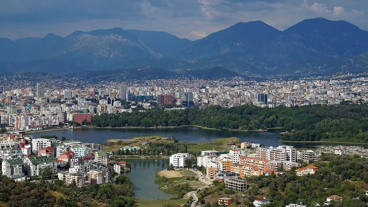 A wide view over the rooftops and towers of Tirana with the surrounding hills behind, the city where most long-stay Americans base themselves