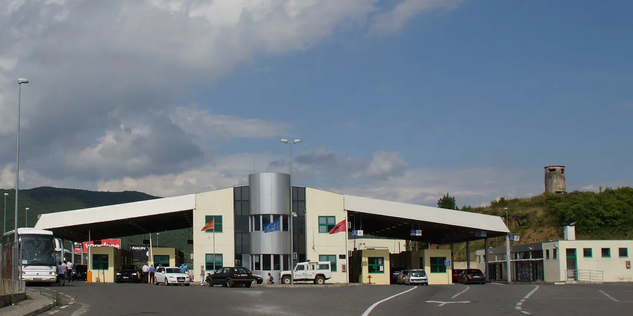 The joint Sukobin-Muriqan border building with Montenegrin, EU and Albanian flags, cars and a tour coach waiting under its canopy