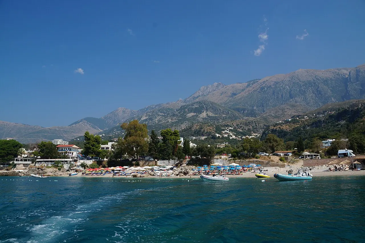 The pebble beach and clear turquoise water at Dhërmi on the Albanian Riviera, with wooded hills behind