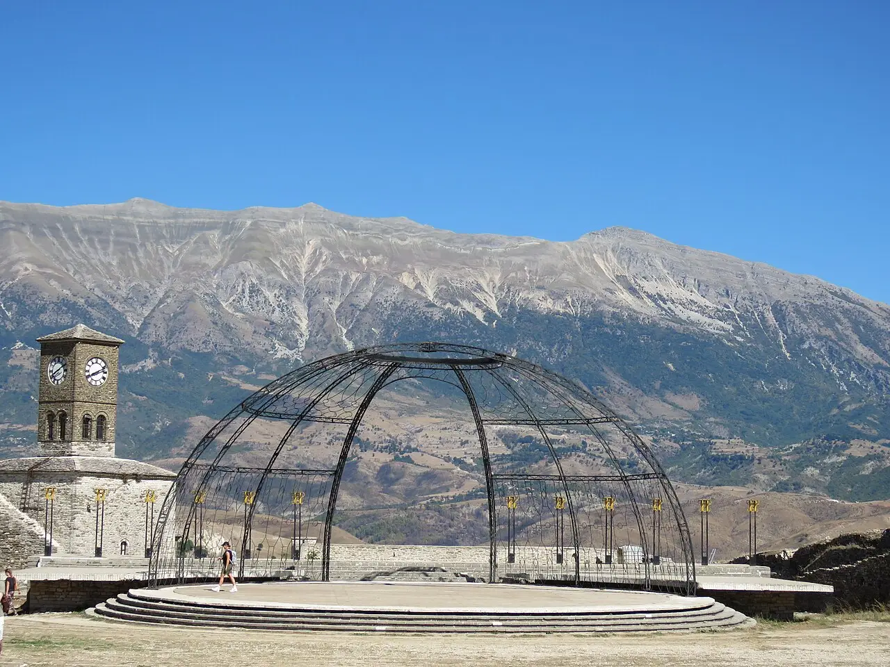 The open-air festival stage and clock tower inside Gjirokastër Castle with the Drino valley mountains behind