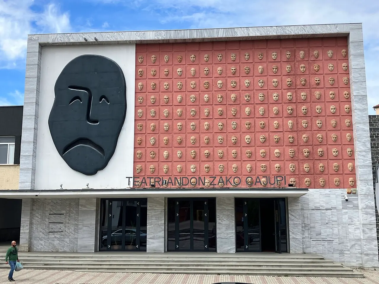 The facade of the Andon Zako Çajupi theatre in Korça, decorated with a large mask and rows of sculpted faces