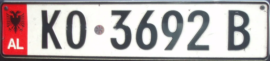 A close-up of an Albanian vehicle registration plate with the red AL band and double-headed eagle