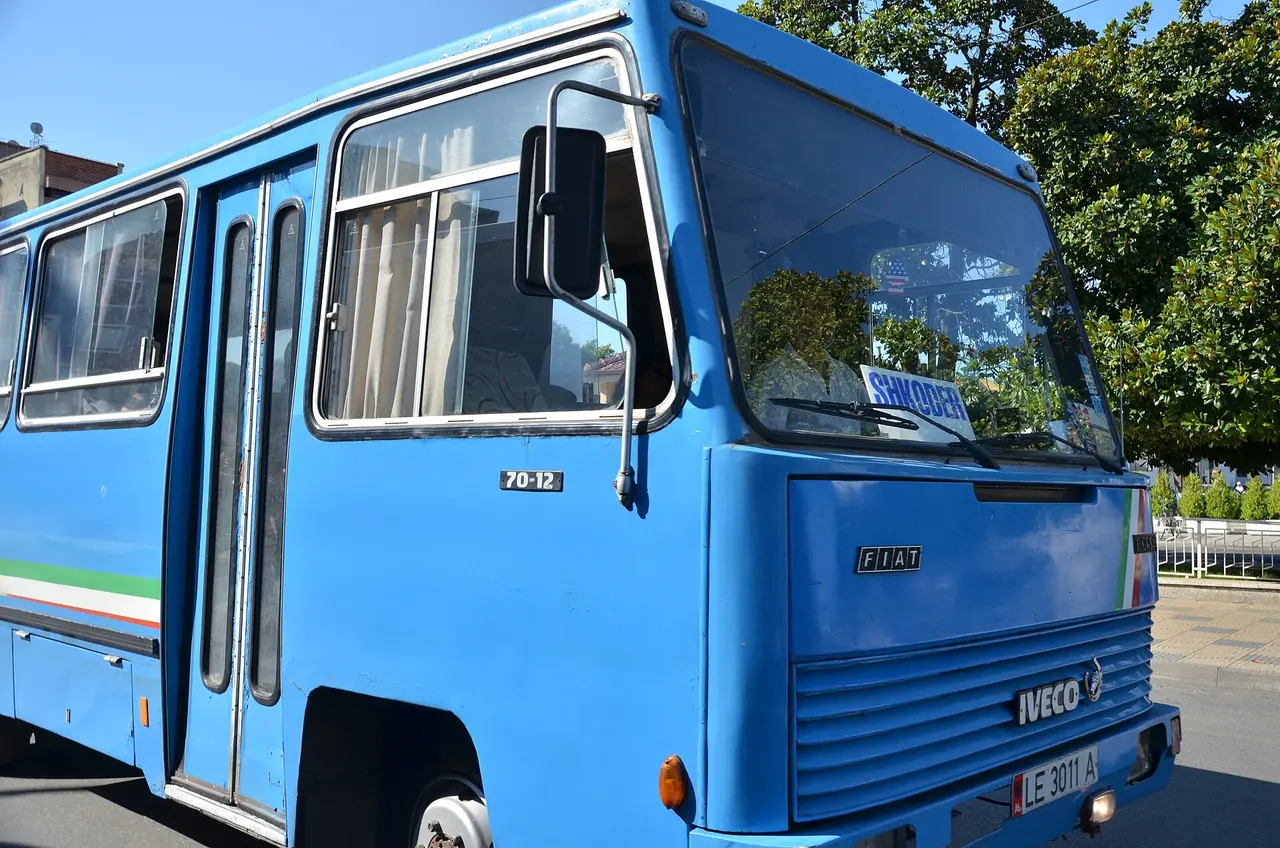 A blue local bus in Albania with a SHKODER destination sign propped in the windscreen