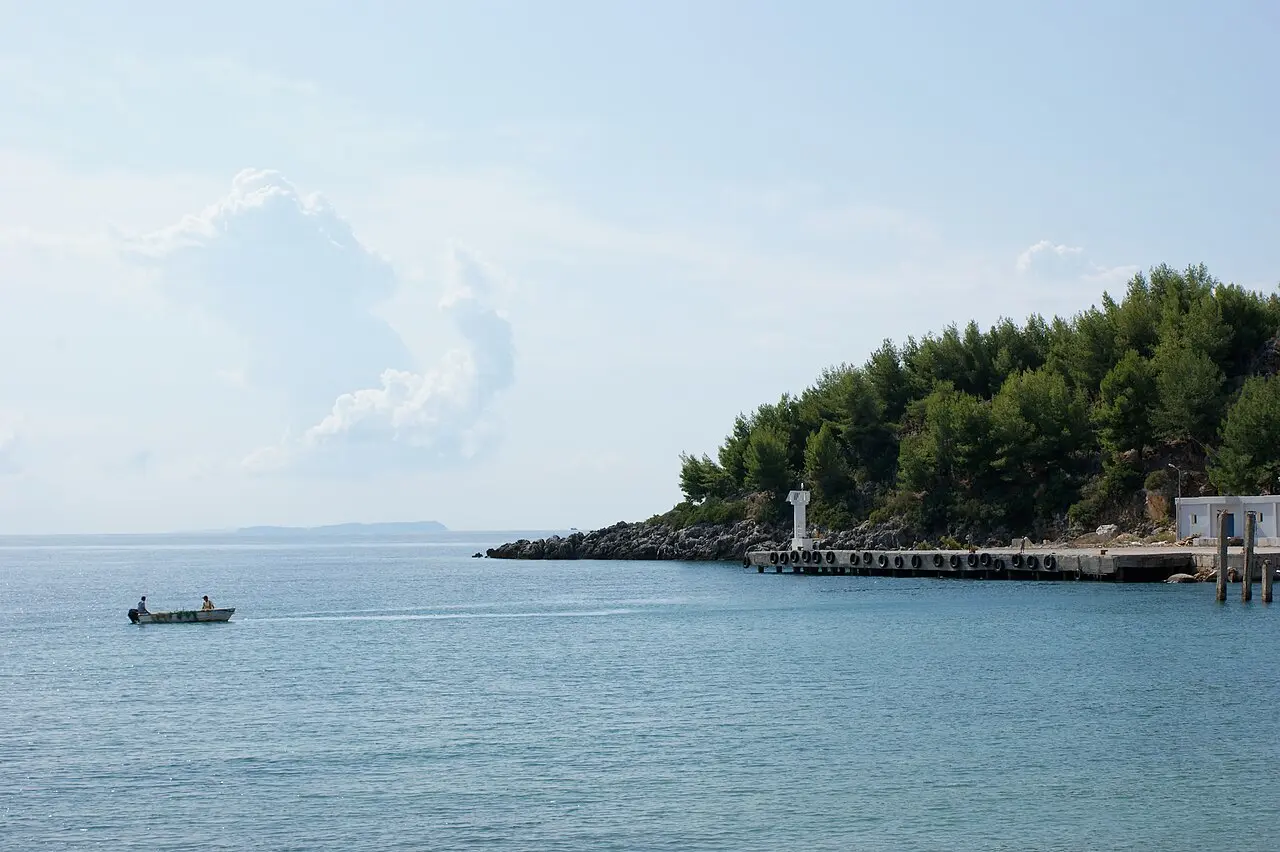 A calm blue bay near Himara on the Albanian Riviera with a small fishing boat and a pine-covered headland
