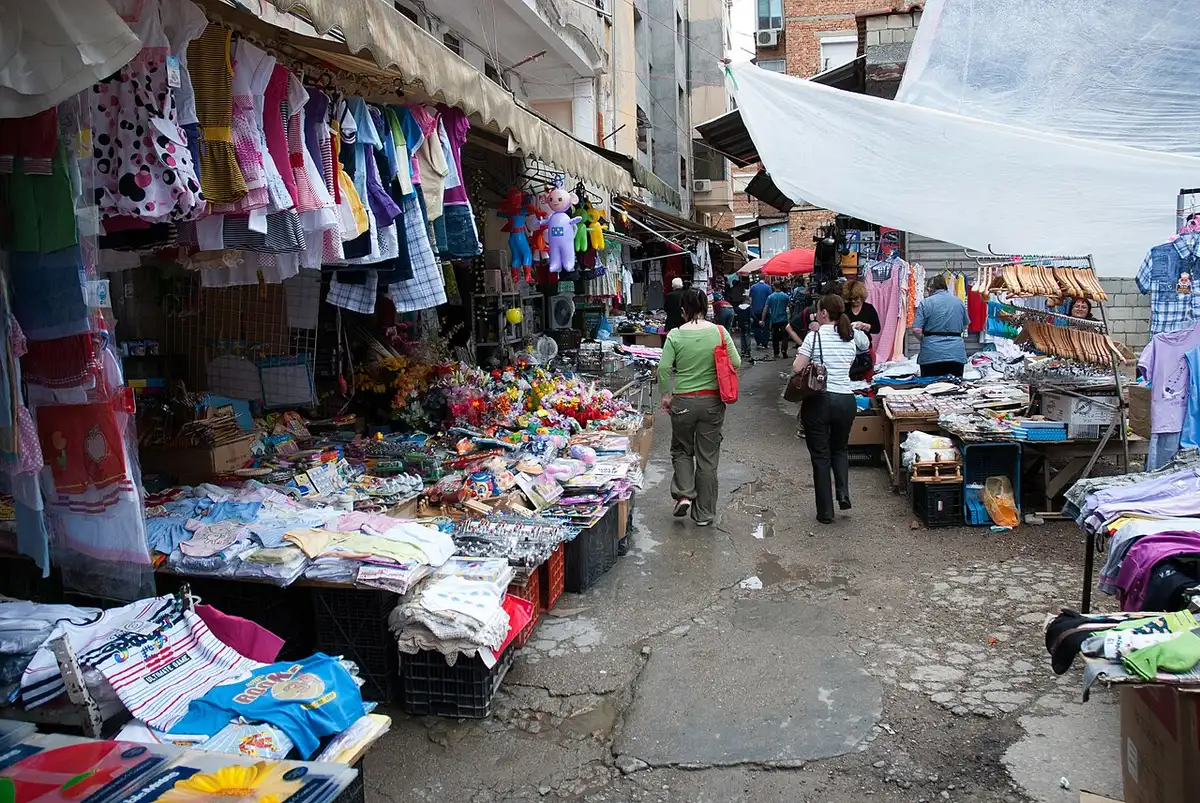 A busy Tirana street market with clothes and household-goods stalls and shoppers browsing between them