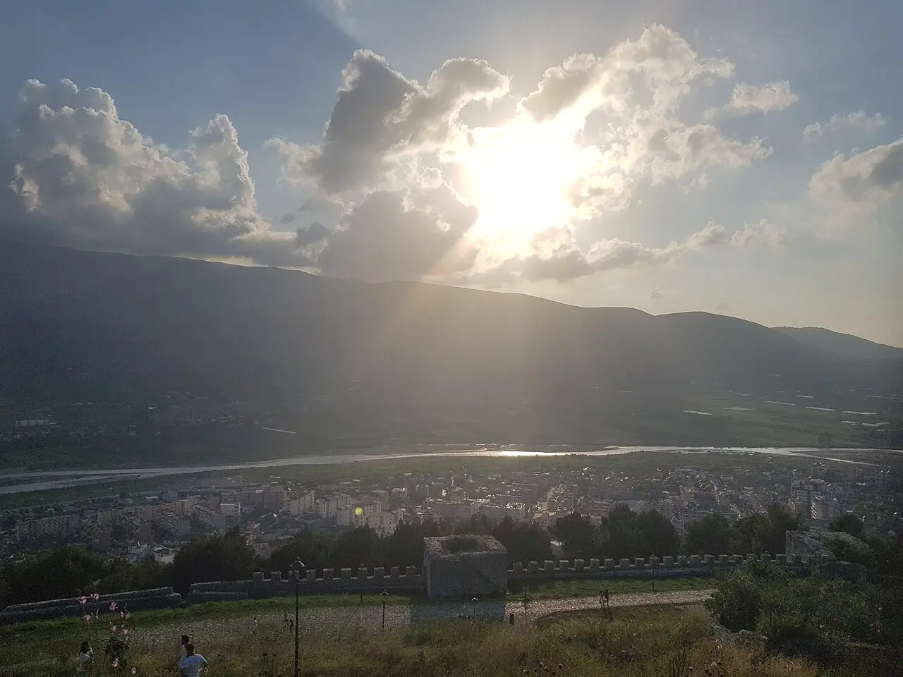 Crenellated stone rampart above Berat looking over the modern town and the river plain in hazy afternoon backlight
