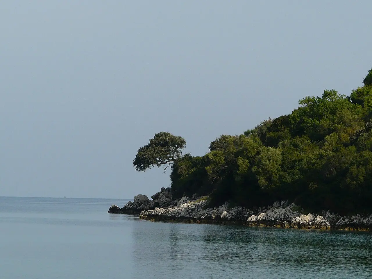 Clear shallow turquoise water and a small green islet just off a Ksamil cove