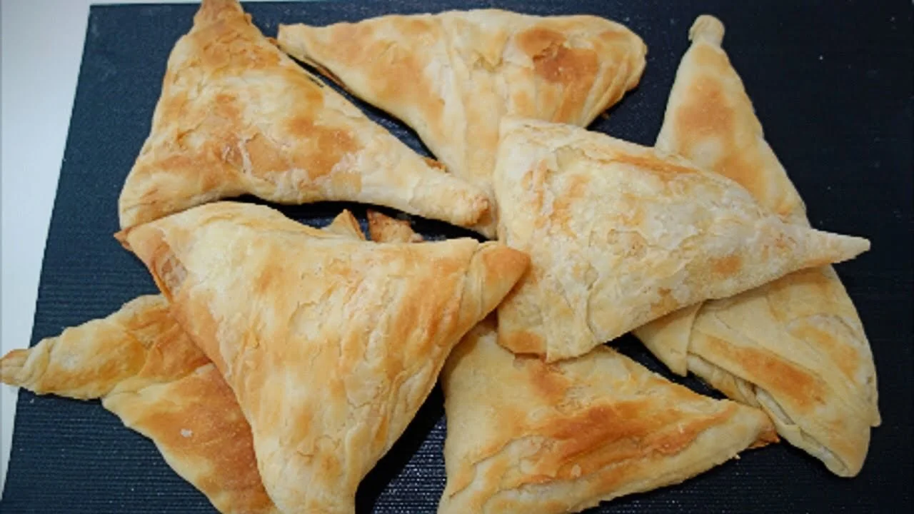 A pile of golden flaky triangular byrek pastries on a dark mat