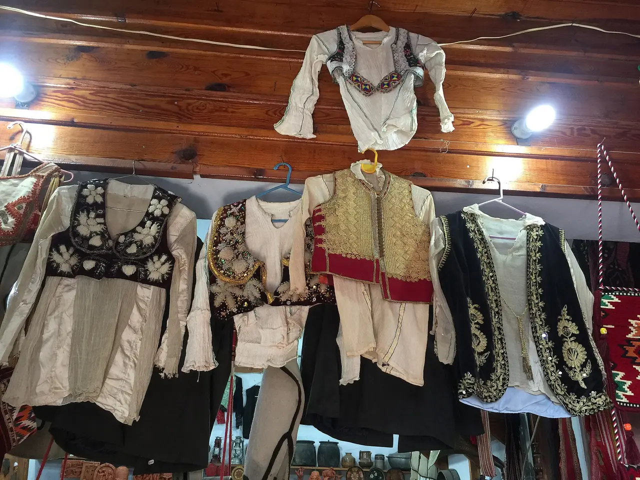 Embroidered folk waistcoats and cotton shirts hanging in a room with a wooden ceiling