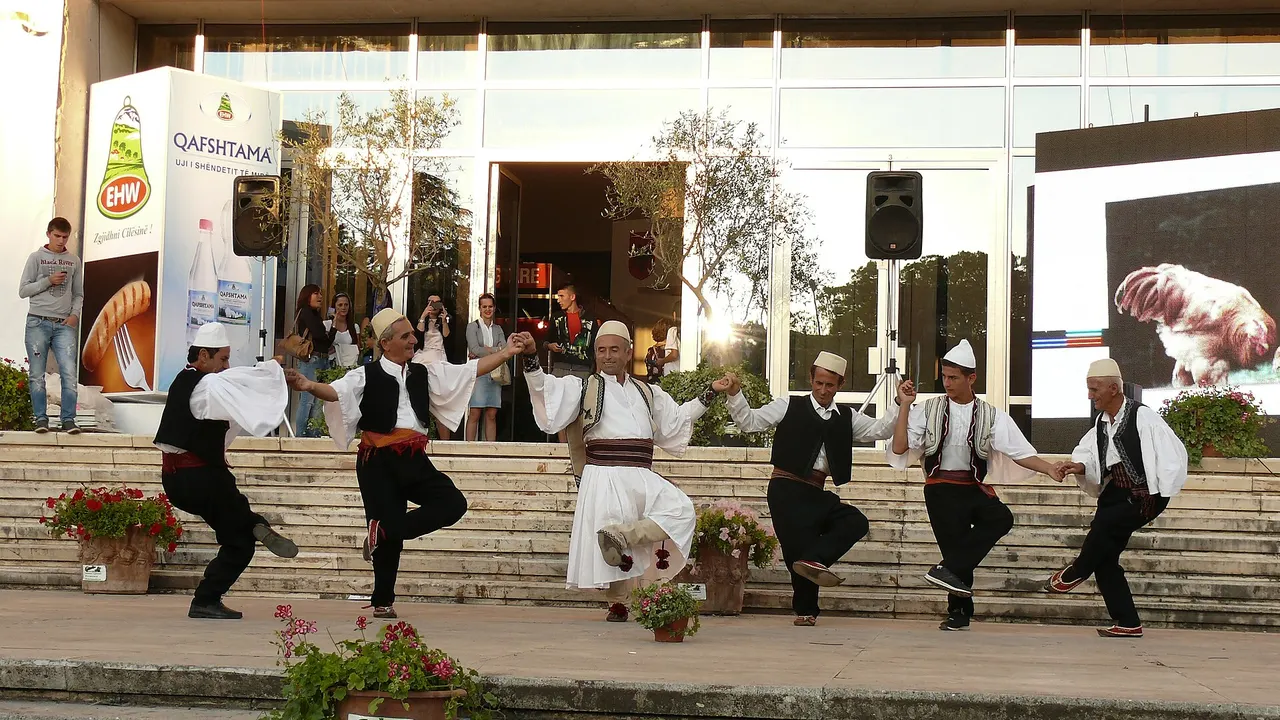 Six men in white shirts and waistcoats dancing a valle hand in hand on an open-air stage