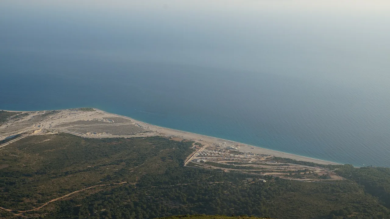 Palasa beach on the Albanian Riviera seen from above, a pale pebble strip and low beach buildings under the Ceraunian hills