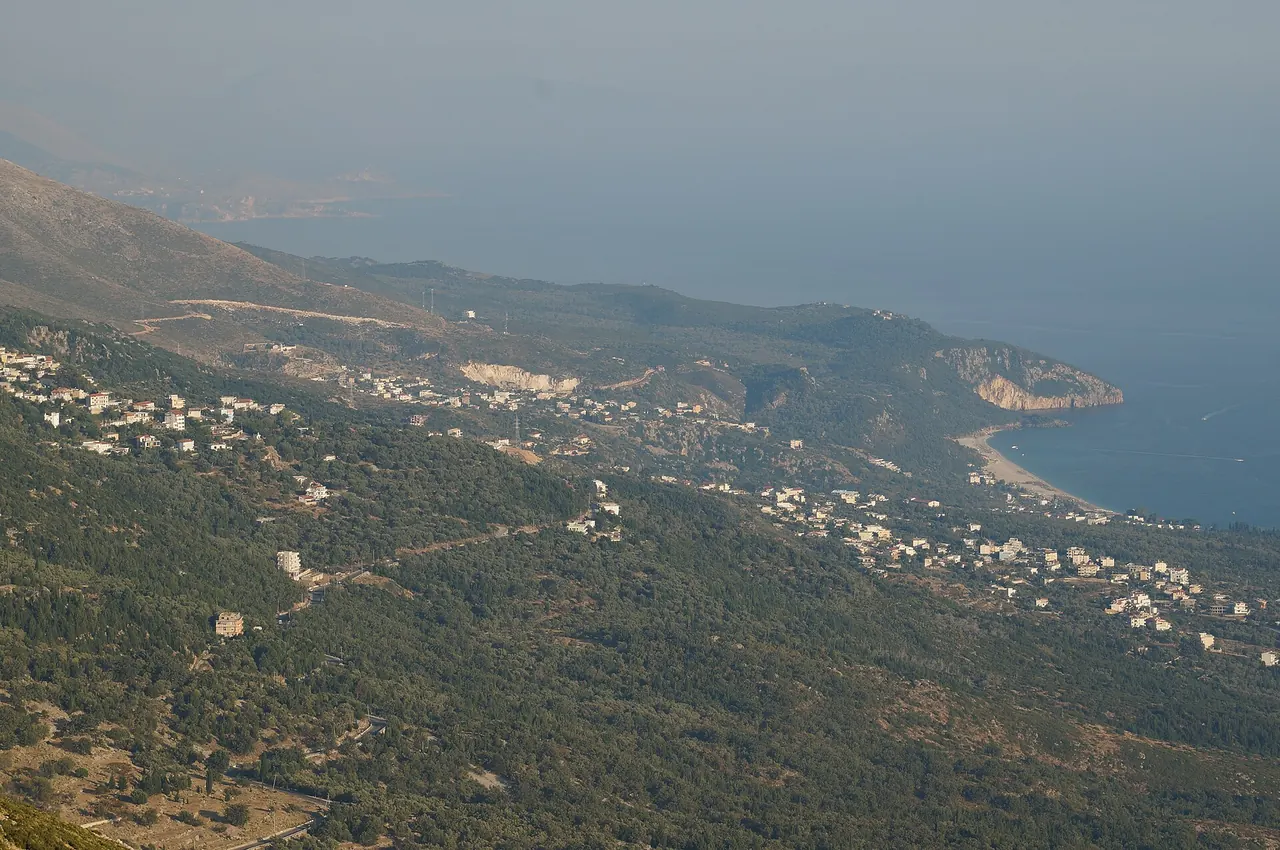 The Dhermi coast seen from the Llogara road, a pale beach curve under green Ceraunian slopes