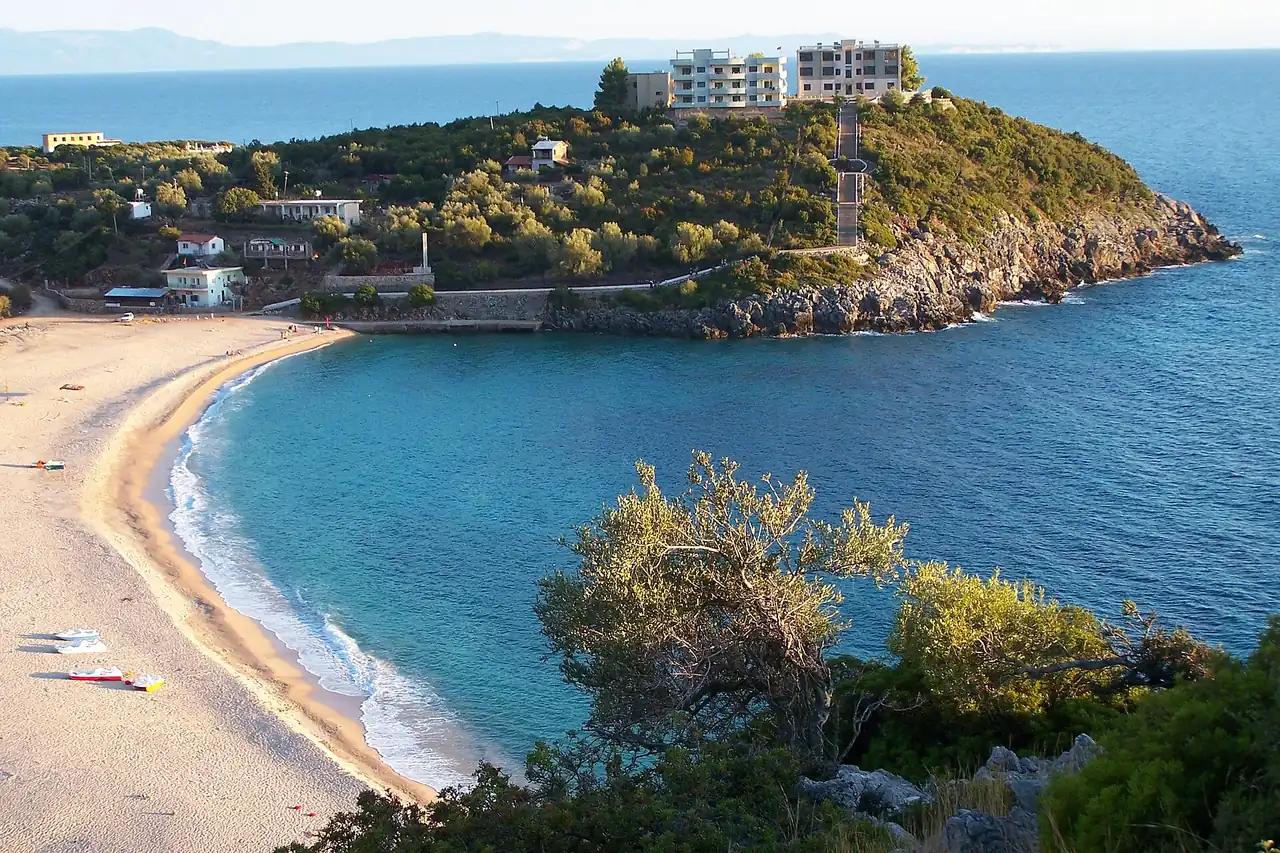 Jale bay on the Albanian Riviera, a turquoise cove with a rocky headland, white buildings and a pale pebble beach