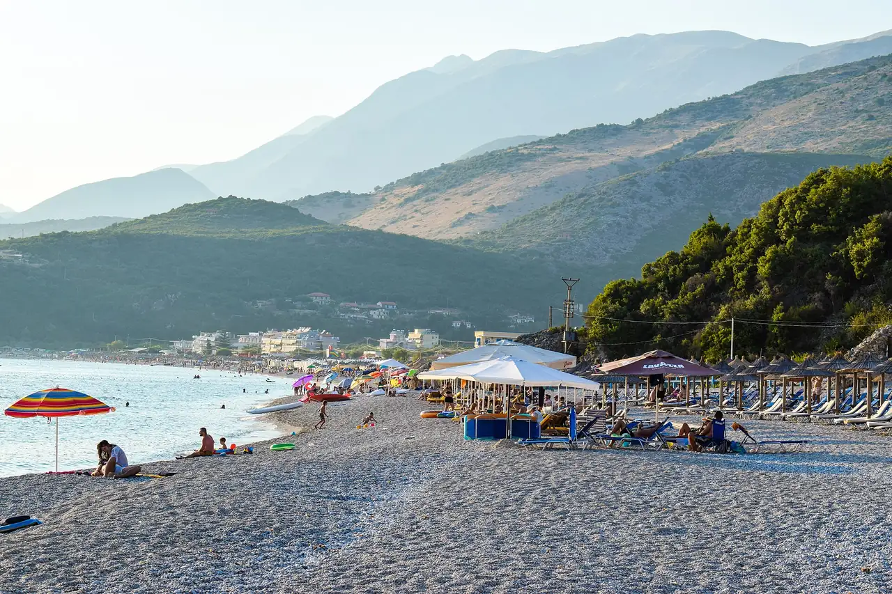 Livadhi beach near Himara with pebble shore, mixed umbrellas, lounger rows and people sitting on free stretches of stone