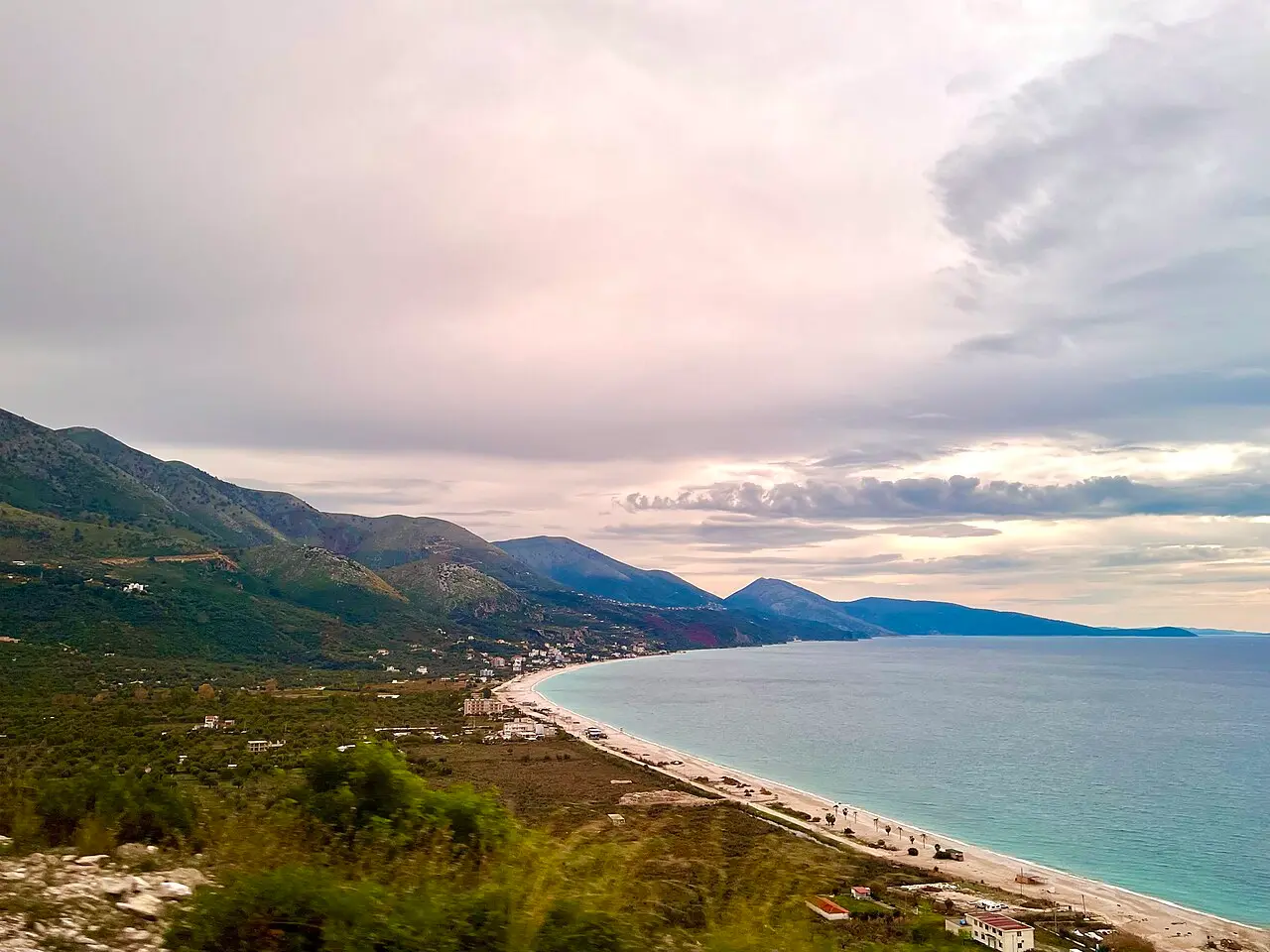 The long sweeping beach at Borsh curving along the coast below green mountains under a soft evening sky