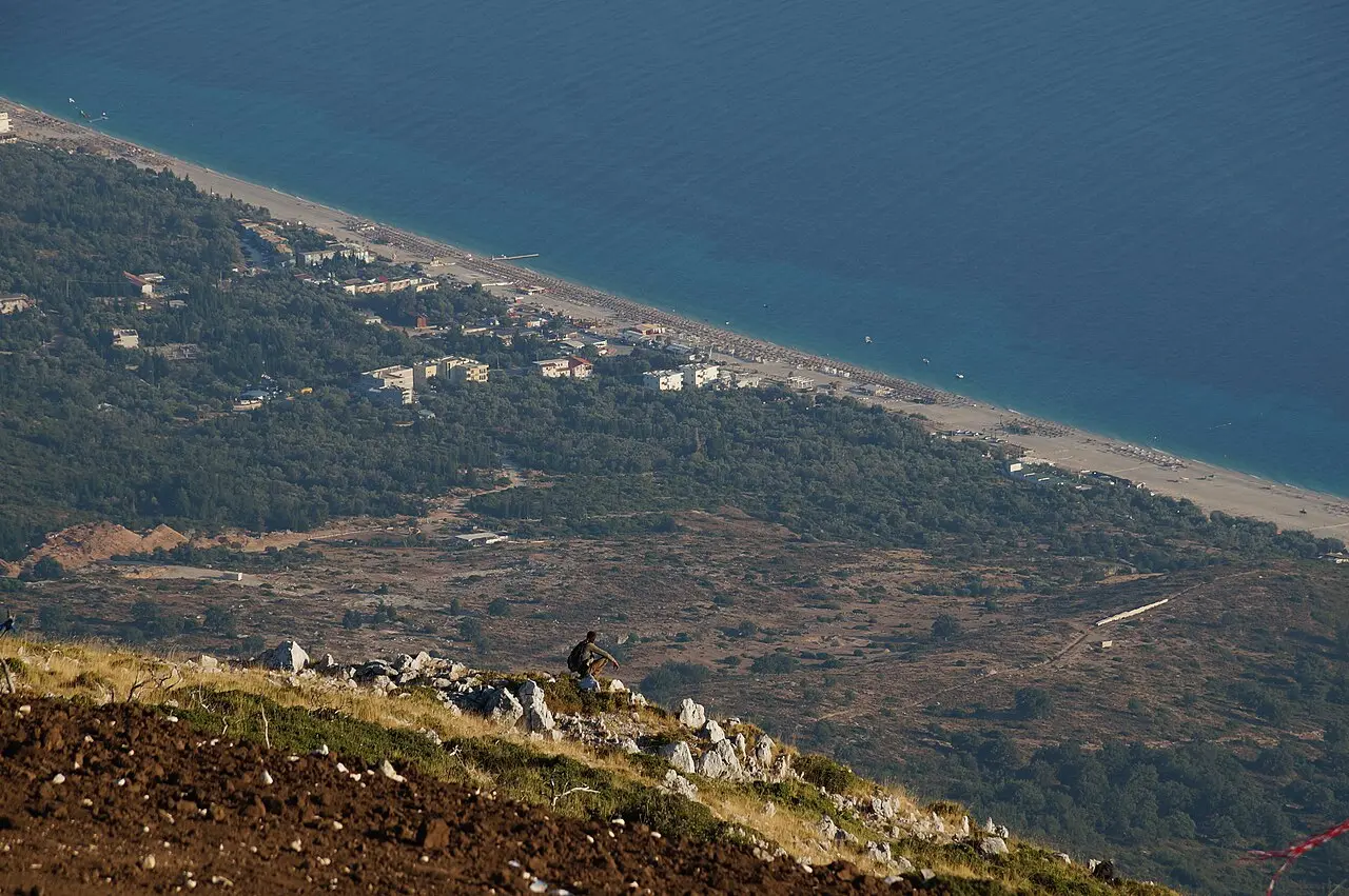 The Dhermi and Drymades beach strip seen from the Llogara descent, the pale beach running along the turquoise Ionian below