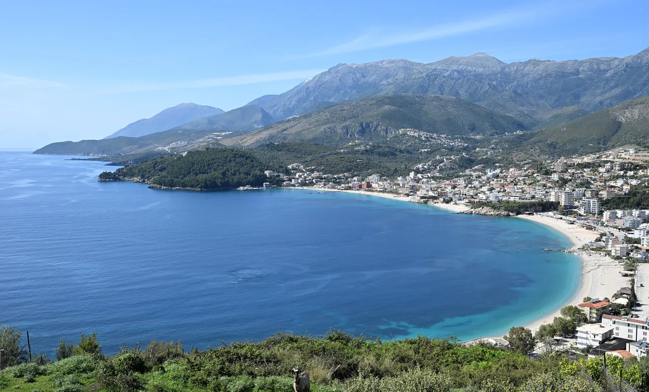 Himara town and its curving turquoise bay seen from the south, the beach and promenade below the Ceraunian Mountains