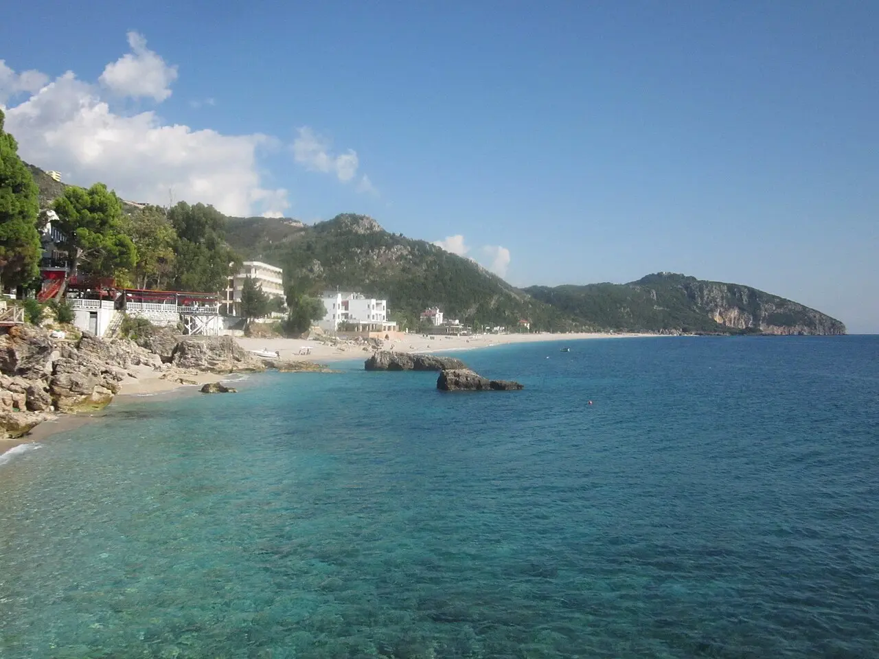 The clear turquoise water and pebble shore of Dhermi beach backed by green hills