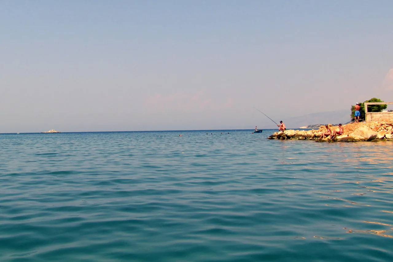 Clear turquoise water and a rocky point at Ksamil, with a swimmer and a small boat just offshore