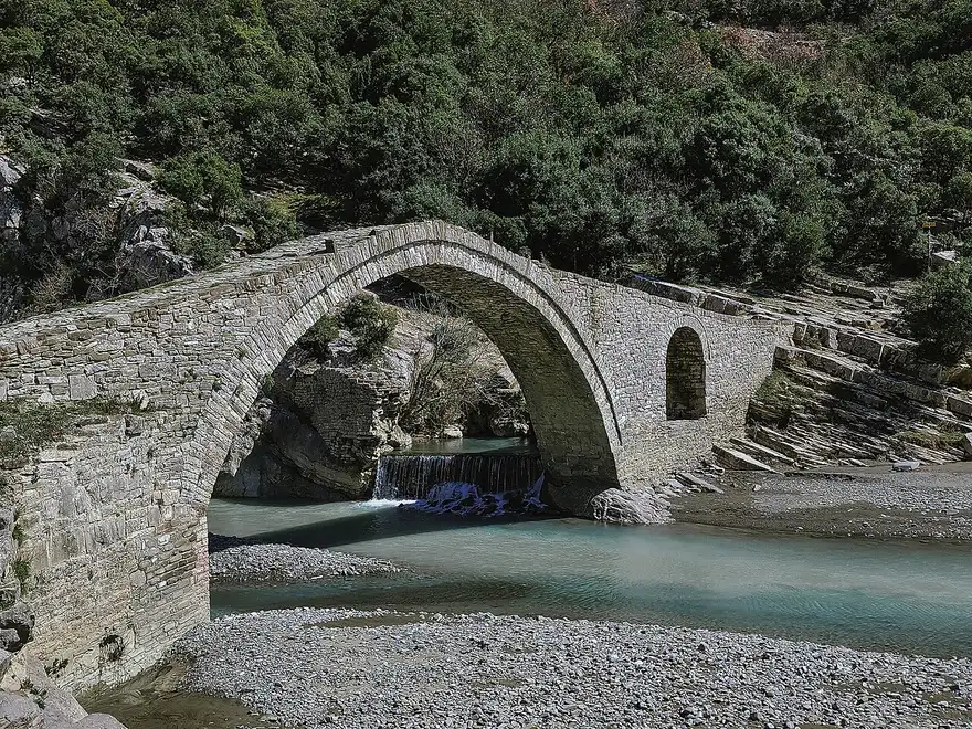 Close view of the single stone arch of the Kadiu Bridge with a small weir and pale blue water beneath