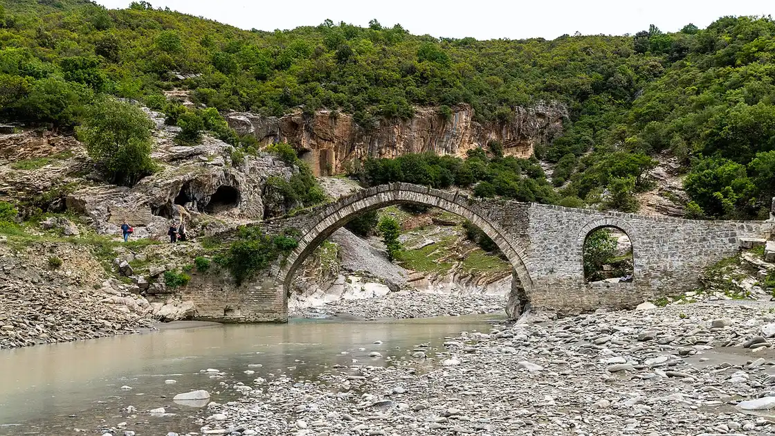 The Ottoman stone Kadiu Bridge over a shallow, wide stretch of the Lengarica riverbed at Benje