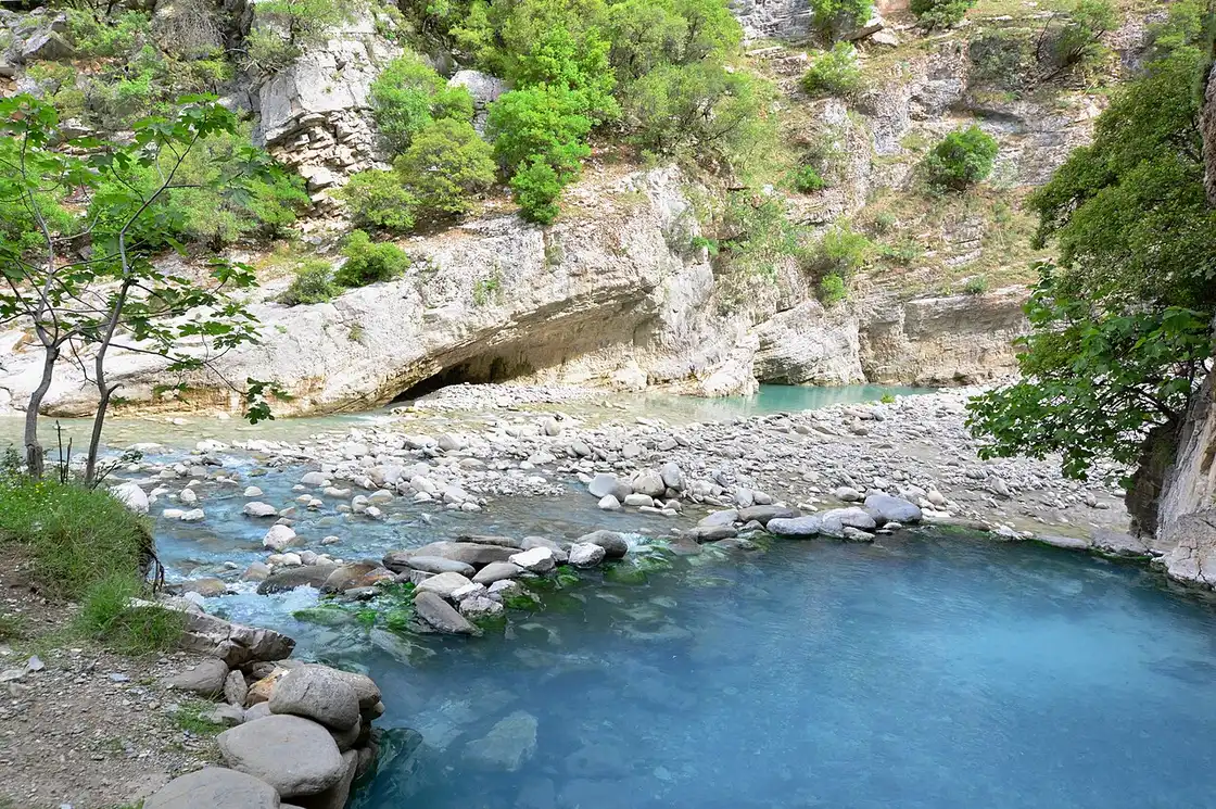 A milky blue thermal pool dammed with stones beside the Lengarica river at the mouth of the canyon