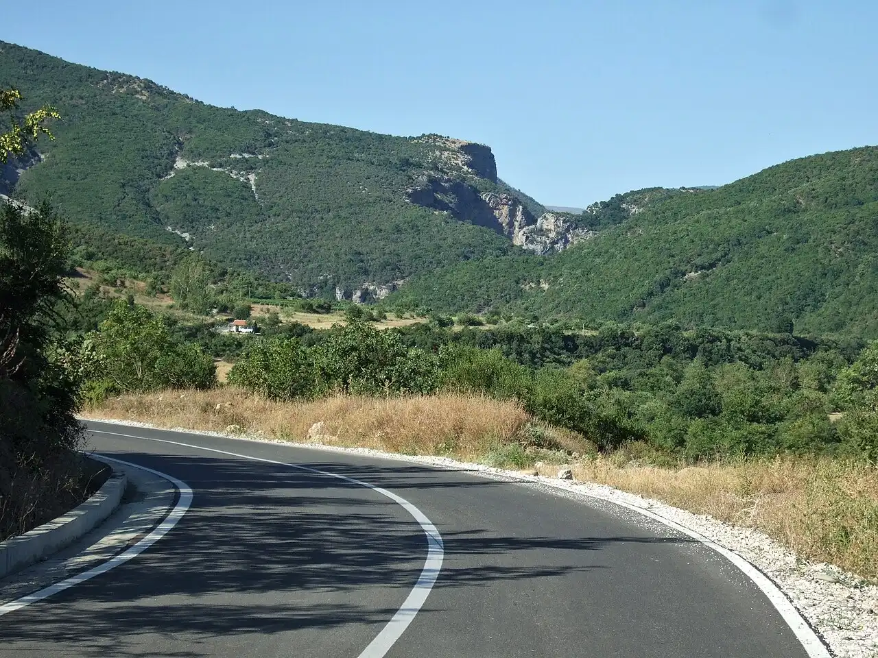 A newly surfaced road curving through green hills towards the rock notch where the Lengarica cuts its canyon