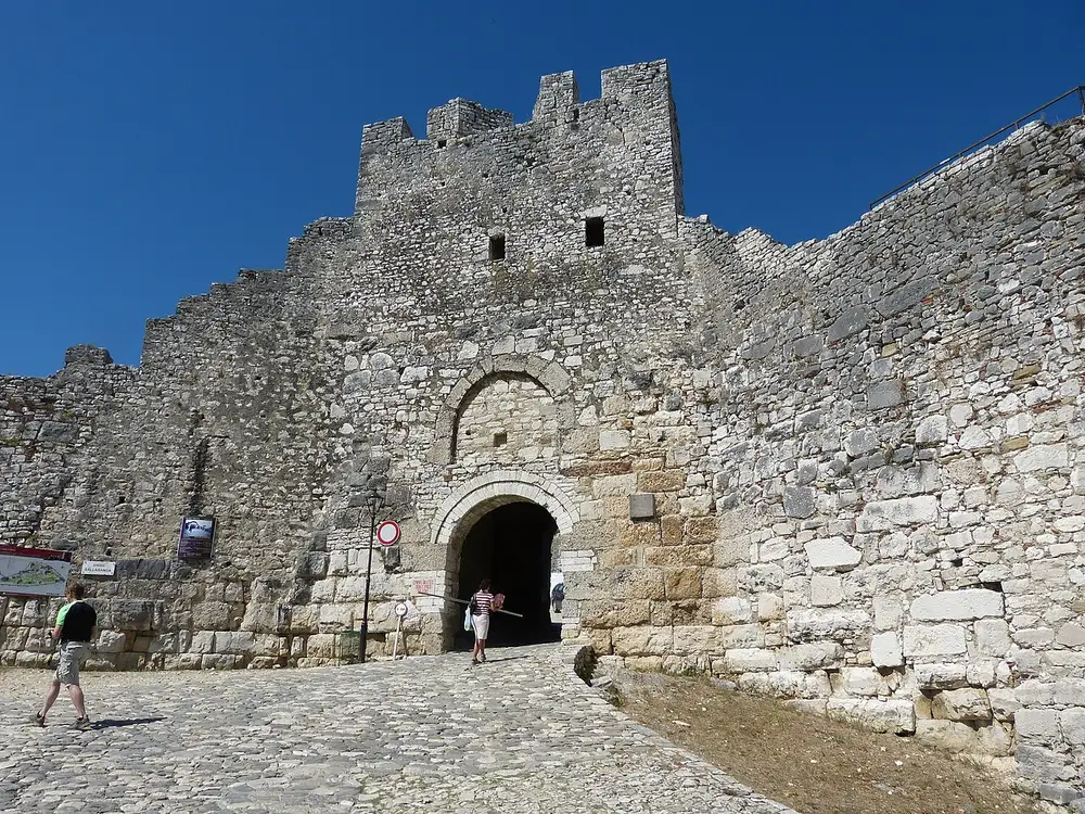 The main stone gateway and crenellated walls of Berat Castle under a blue sky