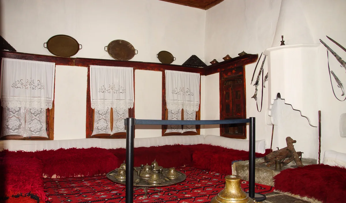 A furnished guest room with red cushions, copper trays and a fireplace in the Ethnographic Museum in Berat