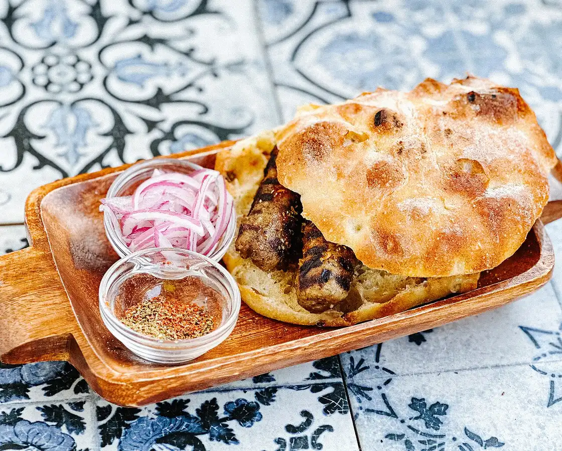 Grilled Albanian qofte meatballs served in bread with raw onion