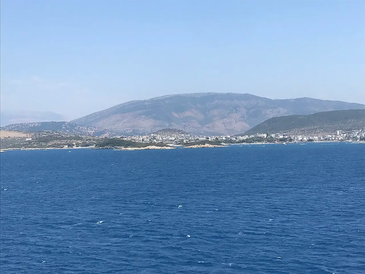 Deep blue summer sea off the Ksamil coastline, with the town and hills in the distance