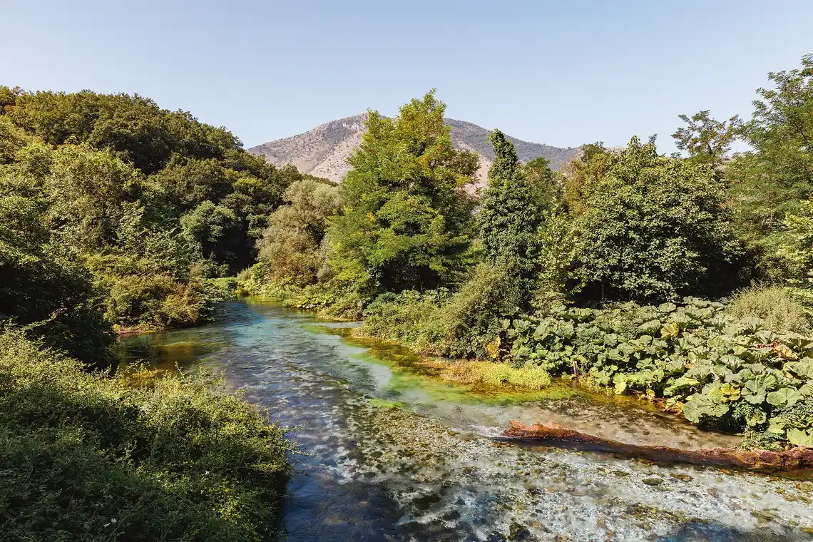 The clear Bistrica river flowing away from the Blue Eye spring through green banks