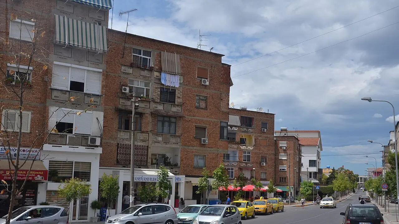 Mid-rise apartment blocks and shops along a busy street in Tirana with mountains behind