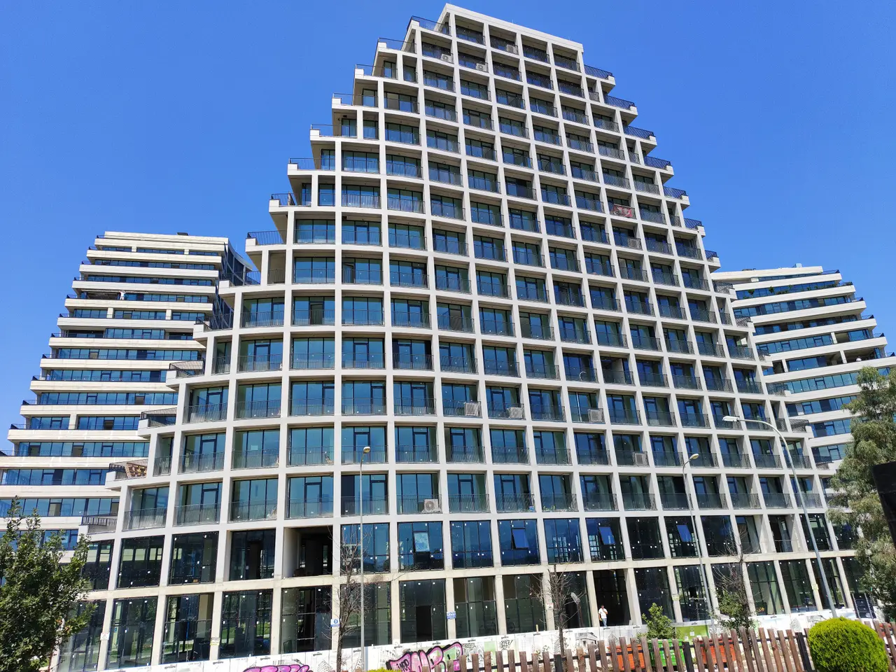 A modern glass-fronted apartment tower in Tirana completed in 2023, with terraces stepping back toward the roofline