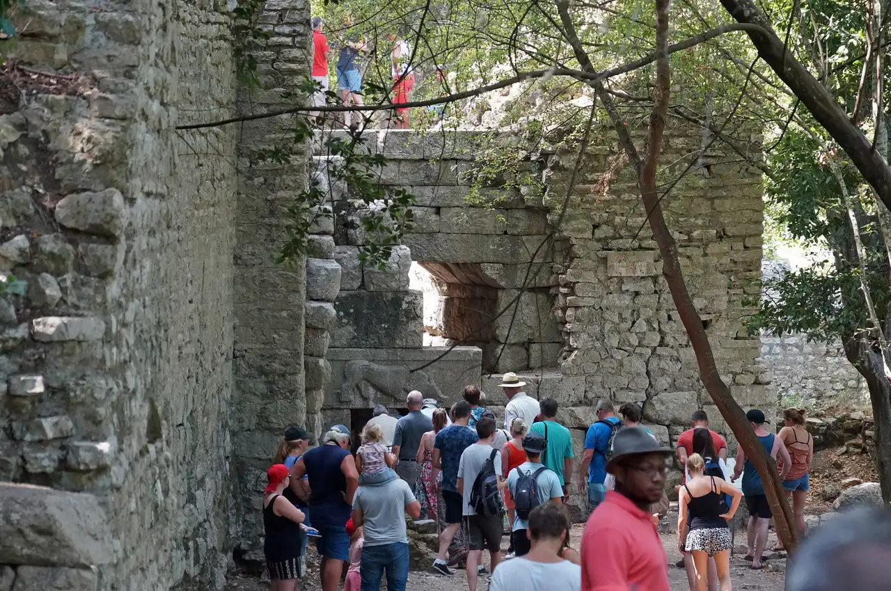 A tour group gathered in the shade beside an ancient stone gateway in the walls of Butrint