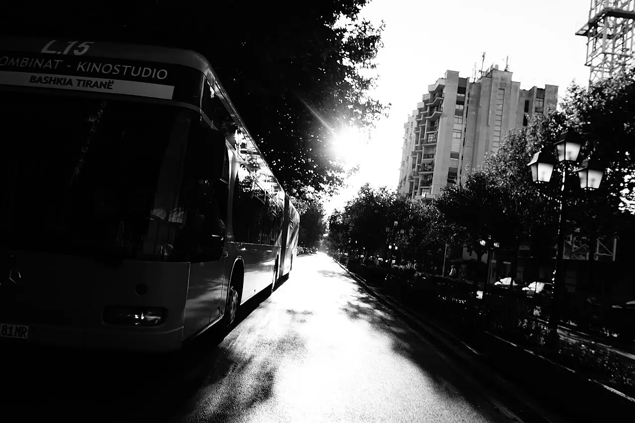 A Tirana municipal bus on route L15 to Kombinat and Kinostudio on a tree-lined street, in black and white