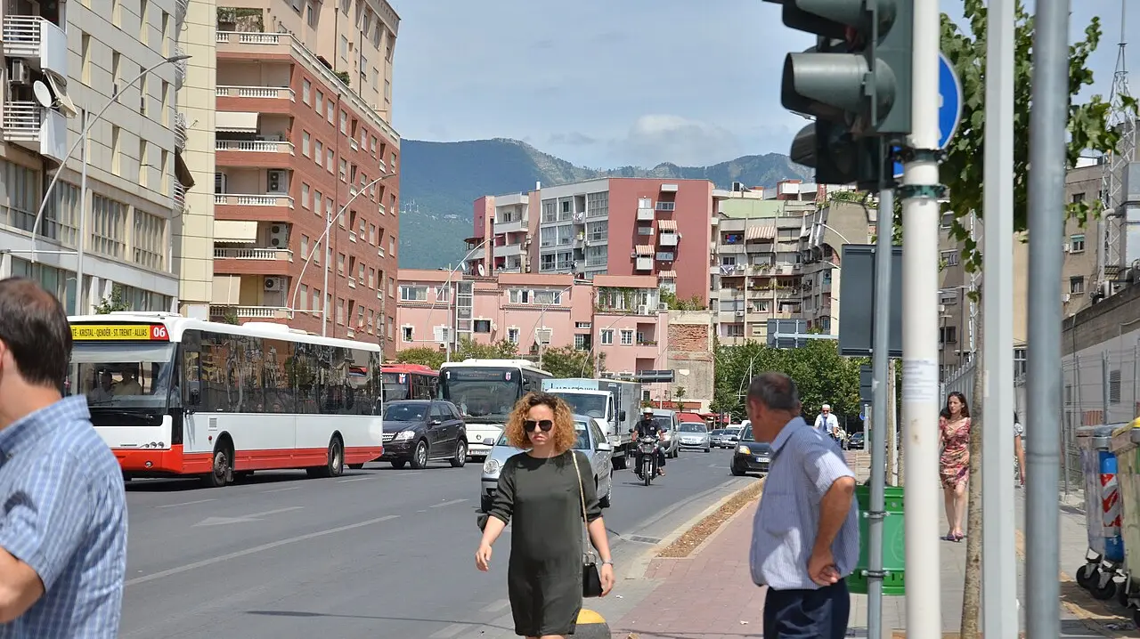 A busy Tirana street with city buses, residential apartment blocks and mountains behind