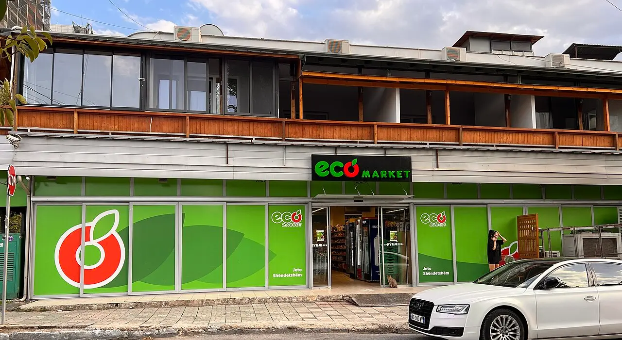 The green storefront of an Eco Market supermarket on a Tirana street in 2025 with a car parked outside