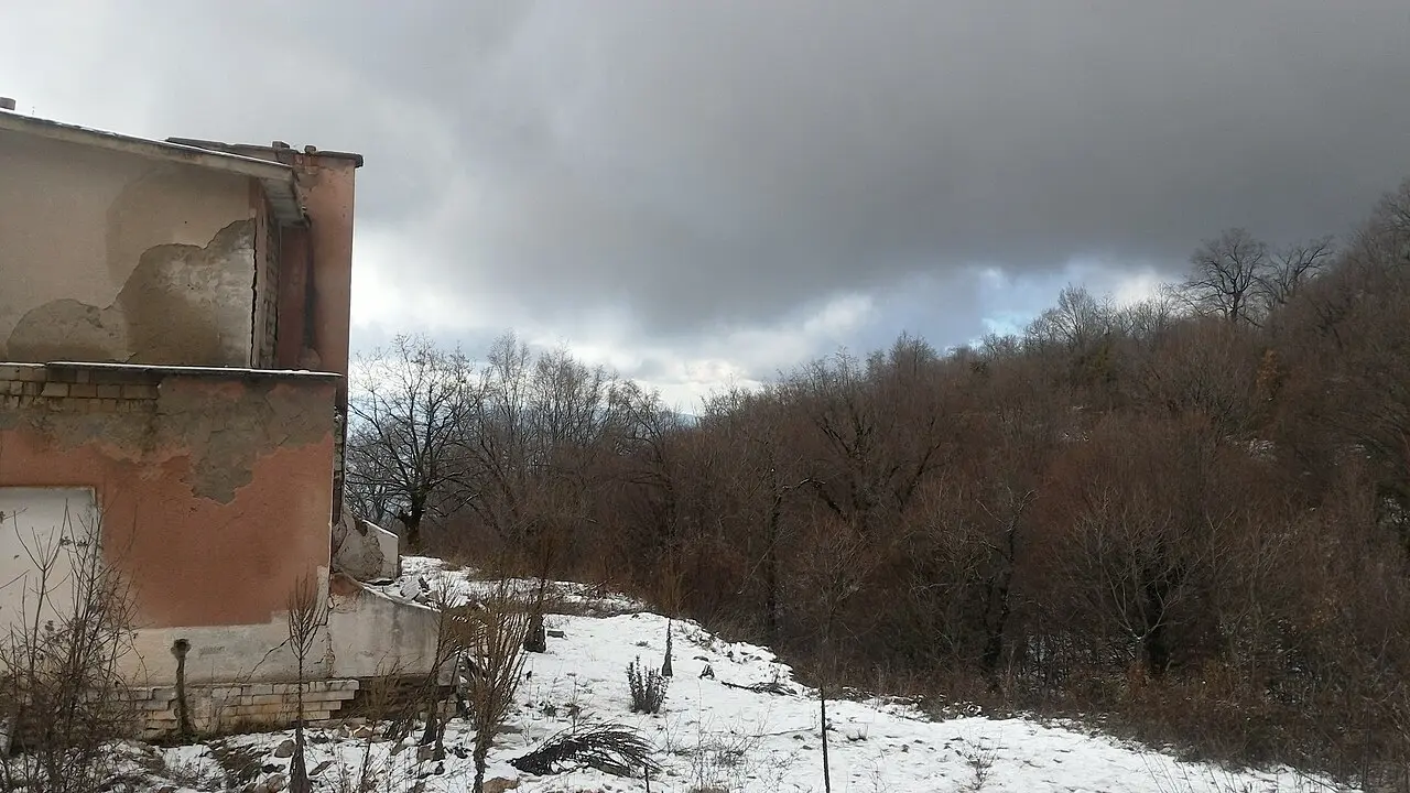A derelict concrete building standing among trees on Mount Dajti