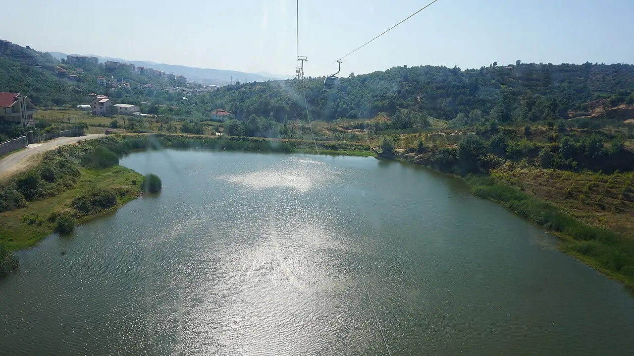 View from a Dajti Ekspres gondola over a green reservoir with the cable line ahead