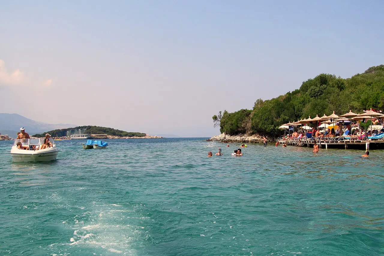 Turquoise water, boats and one of the wooded islets off the beaches at Ksamil