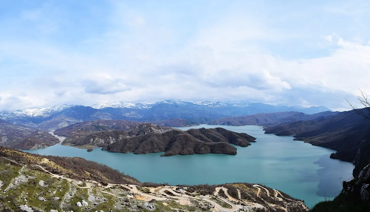 The turquoise water of Lake Bovilla ringed by hills and snow-dusted mountains