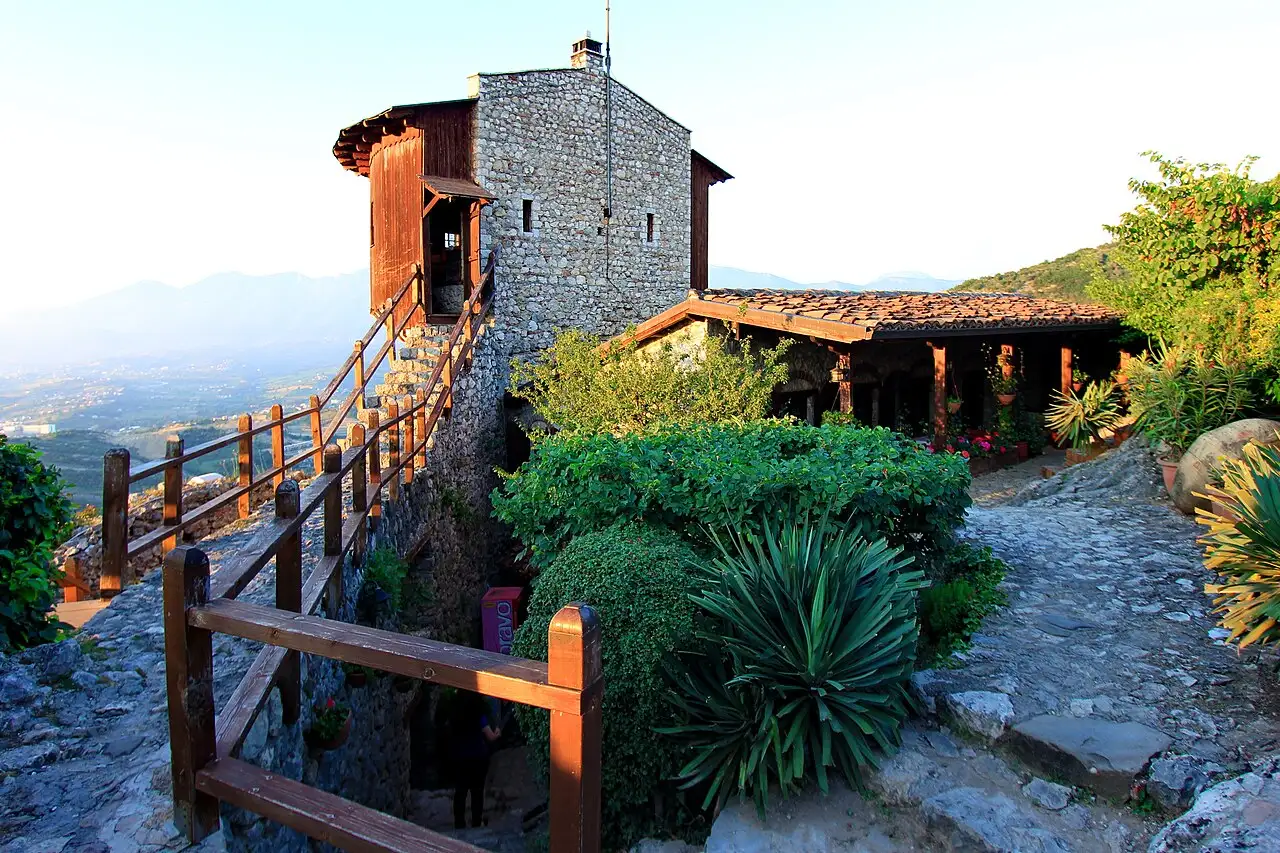 The stone tower and terrace restaurant of Petrela Castle catching low sun above a green valley