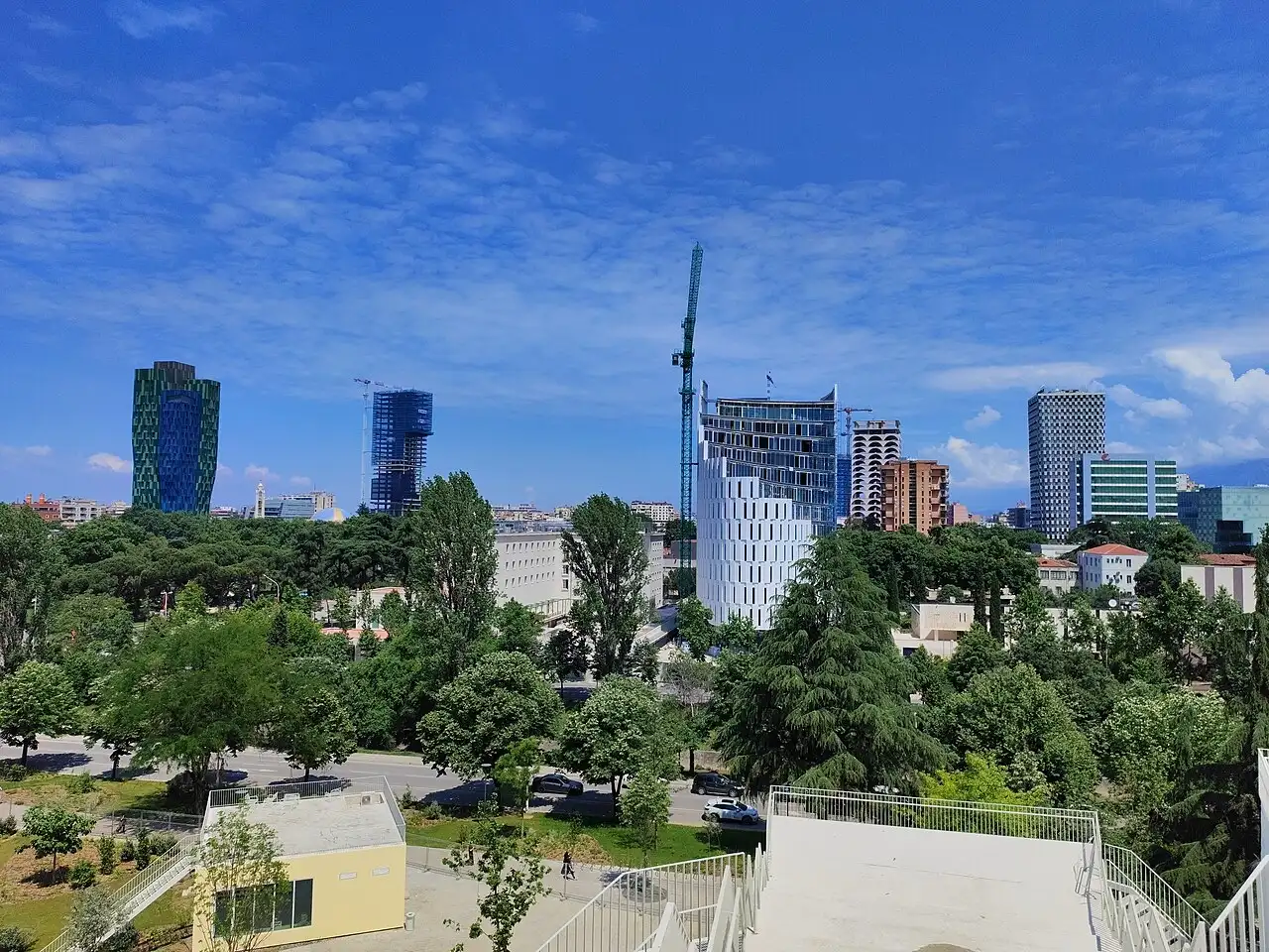 The modern Tirana skyline with the green mosaic tower, new high-rises and leafy parks under a blue sky