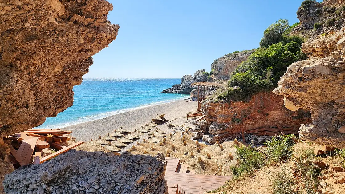 The pebble shore and clear turquoise water of Drymades beach with green hills behind