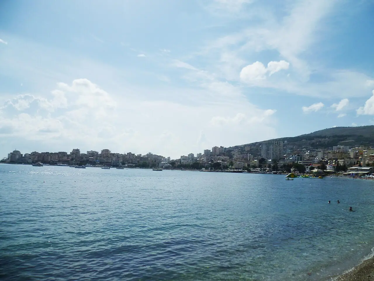 View across the bay at Sarandë, with the town curving around the shoreline and swimmers in the water