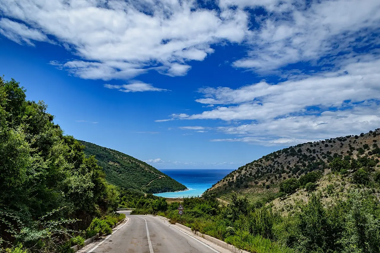 A narrow coastal road winding along a green hillside above the sea near Saranda in southern Albania