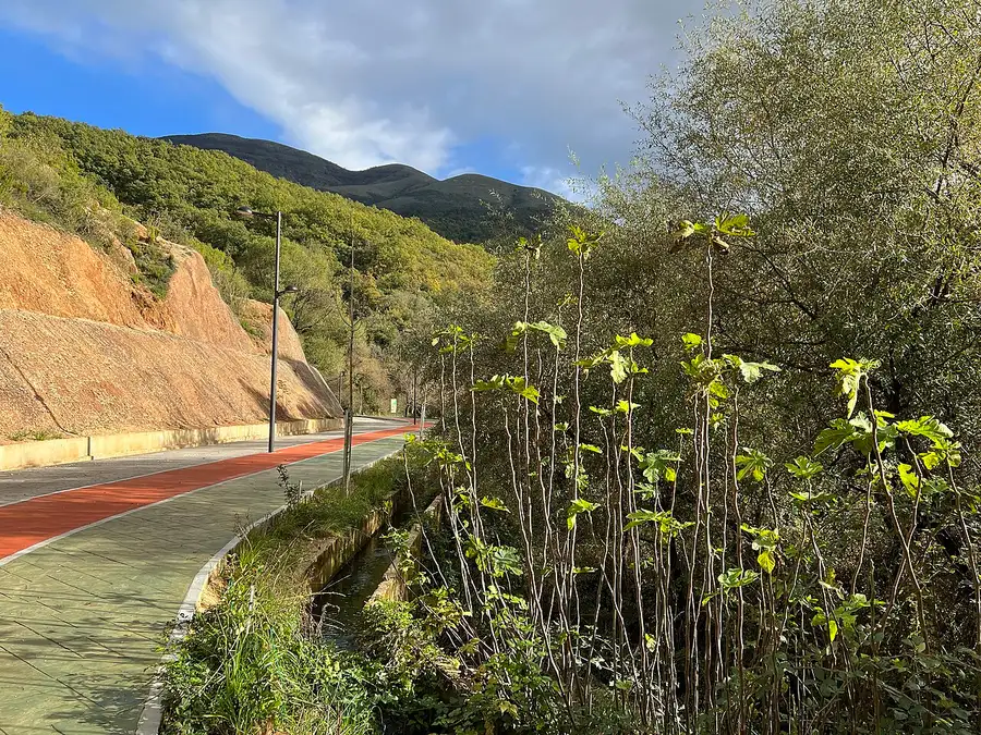 A blind curve on a rural Albanian road climbing a green hillside with no crash barrier