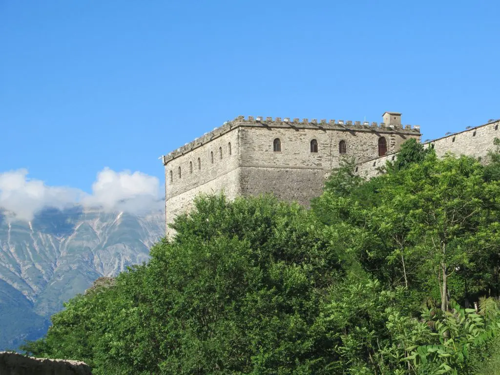 A stone bastion of Gjirokastër castle rising above the trees with hazy mountains behind