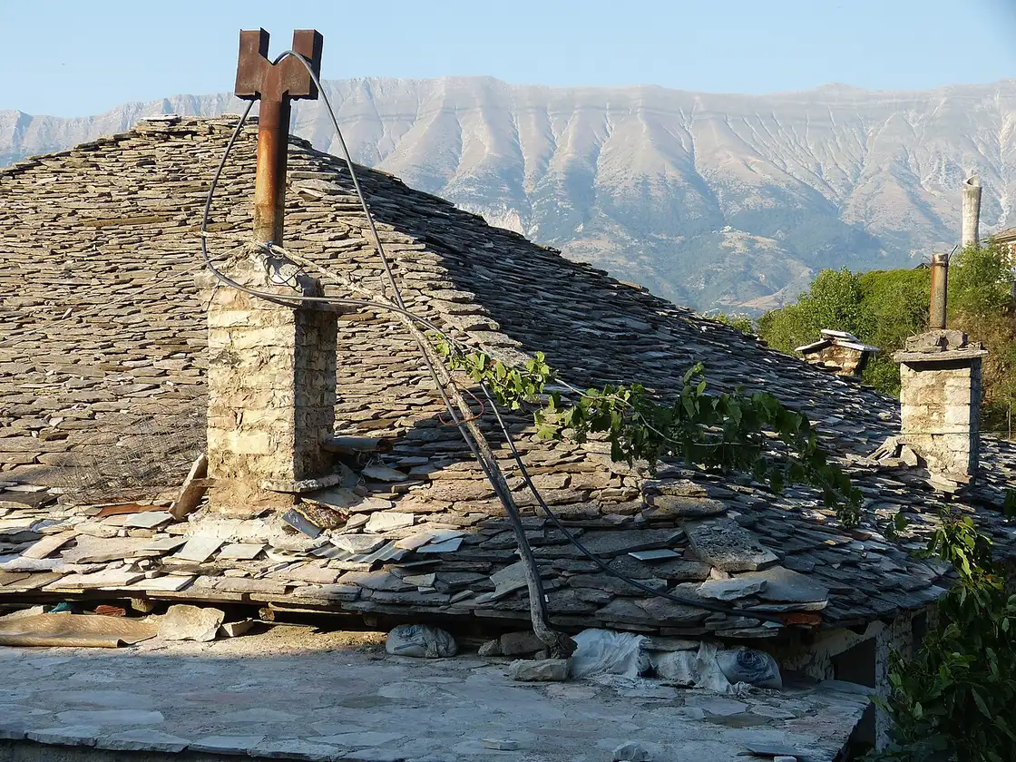 A close-up of the grey stone-slab roof of a Gjirokastër house with the mountains behind